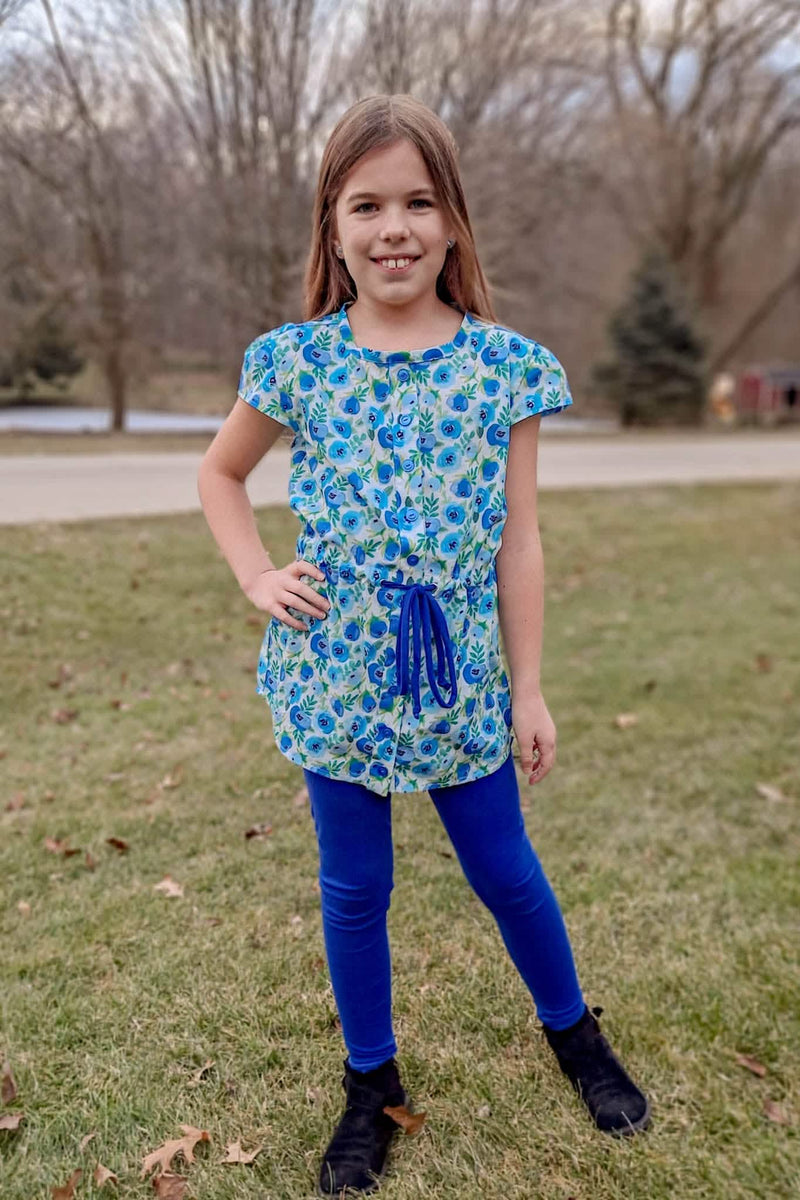 A young girl wears a blue buttercup print top with blue leggings and black boots.