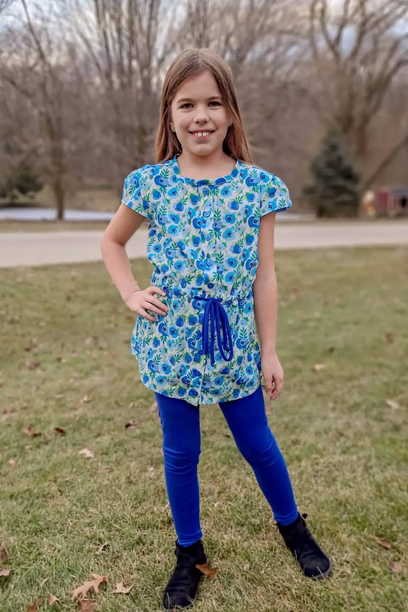 A young girl wears a blue buttercup print top with blue leggings and black boots.