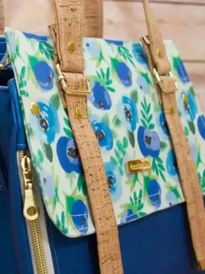 A blue floral fabric bag with cork straps and gold hardware.