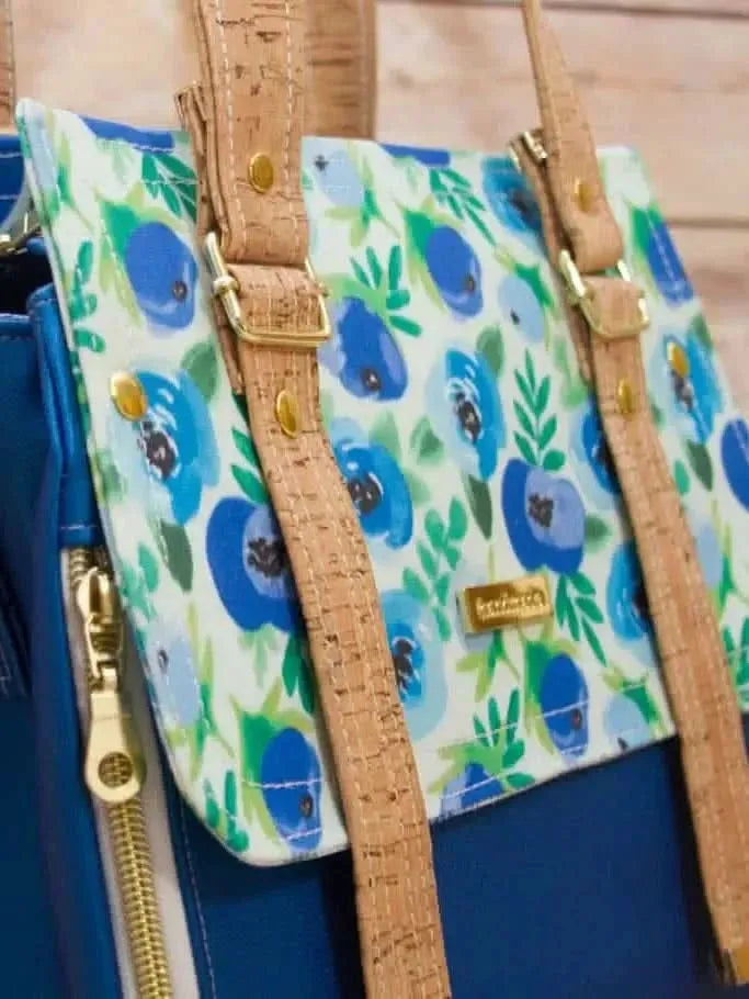 A blue floral fabric bag with cork straps and gold hardware.