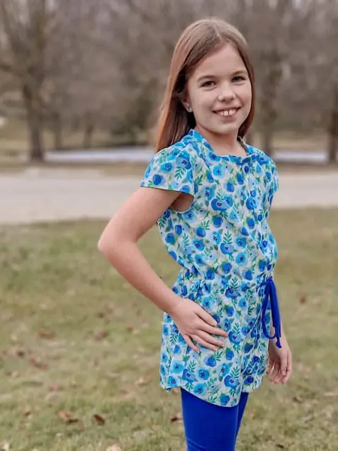 A young girl wears a blue floral top with blue leggings outdoors.