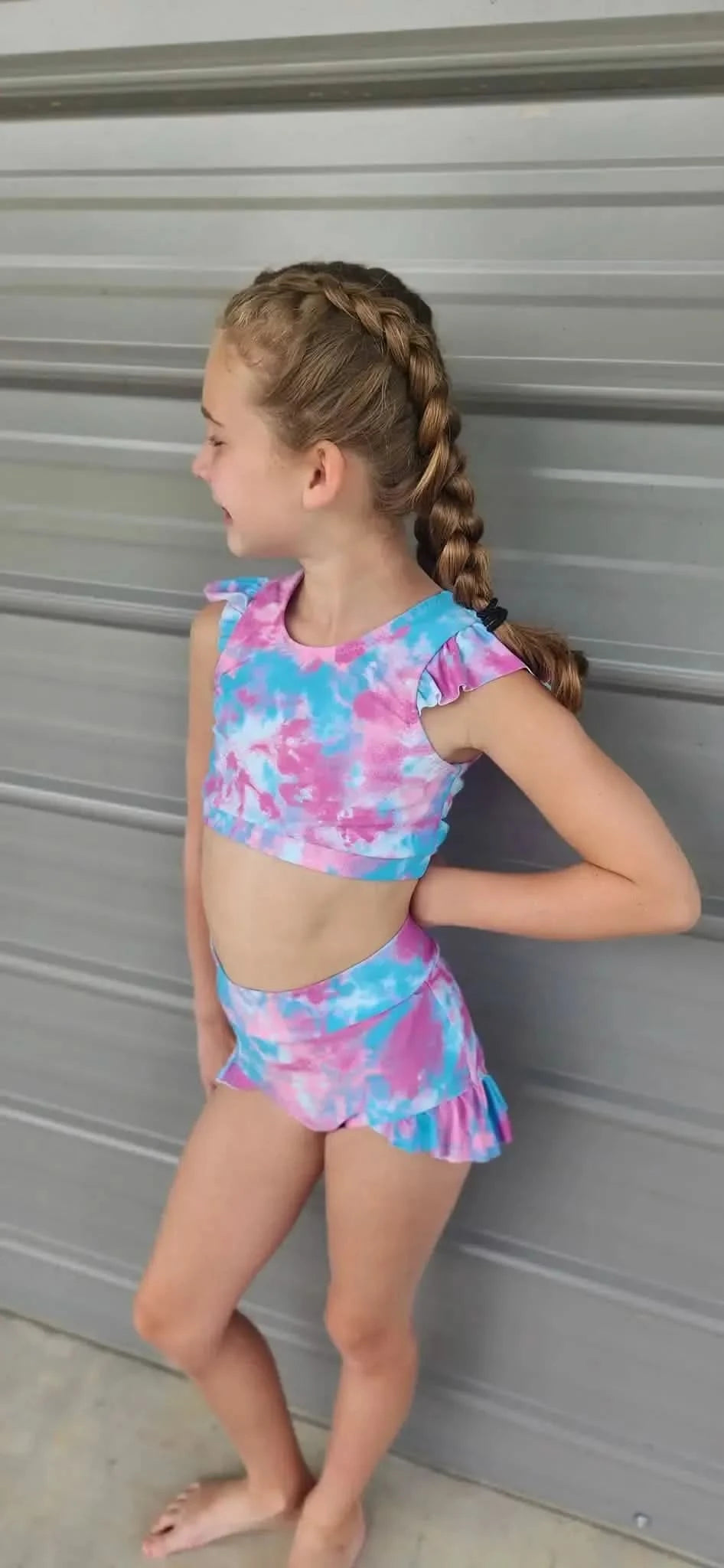 A young girl wears a two-piece mermaid tie-dye swimsuit with ruffled sleeves and skirt.