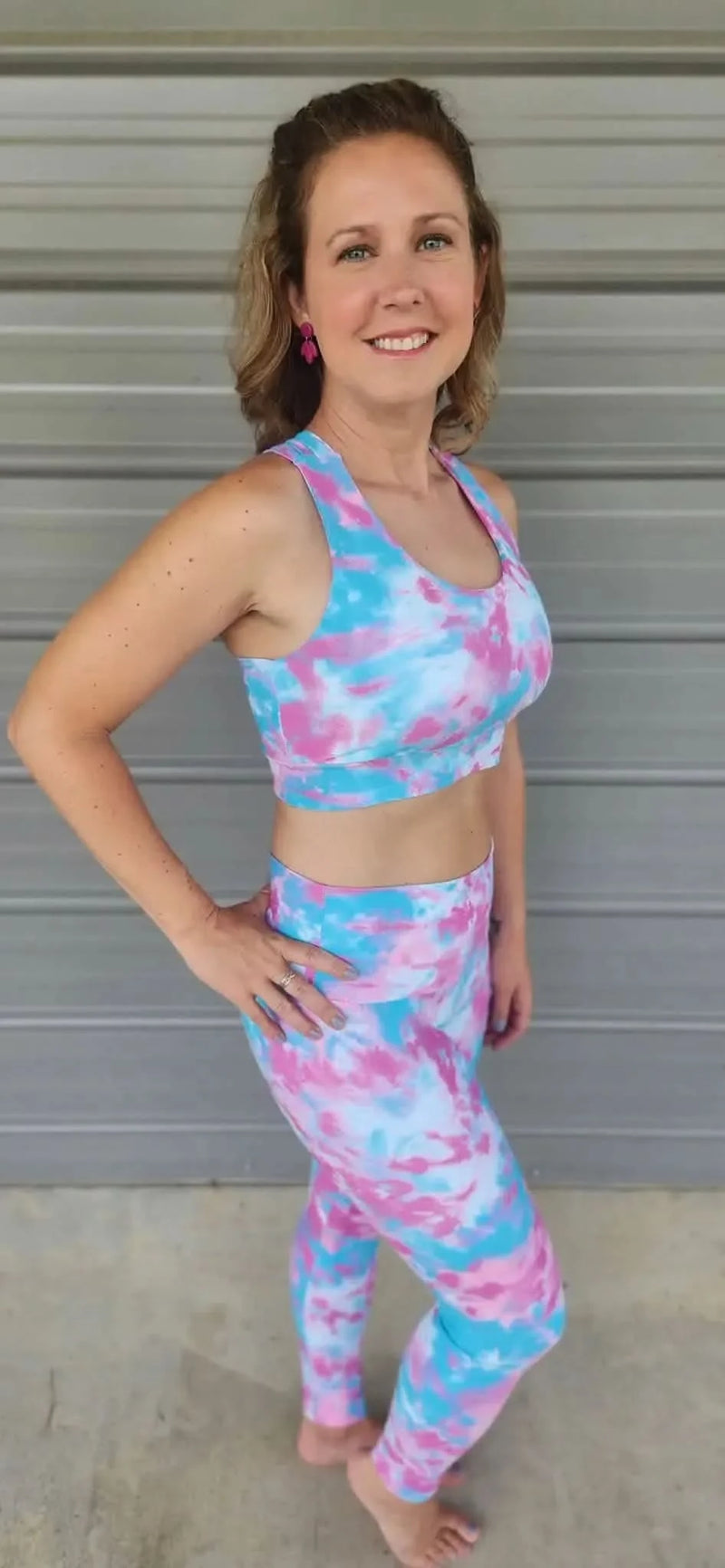 A woman models a tie-dye sports bra and leggings set in pink and blue.