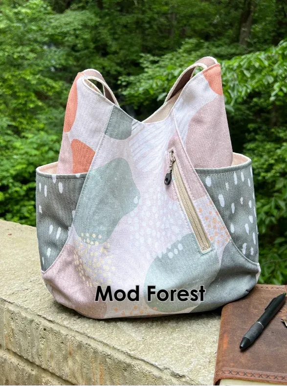 A canvas bag in a Mod Forest pattern with a zipper pocket, resting on a stone ledge.
