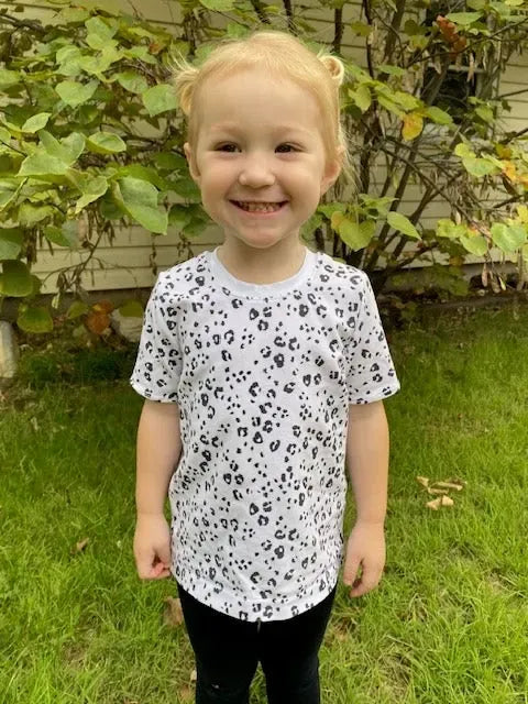 A young child wears a white t-shirt with a black leopard print pattern.