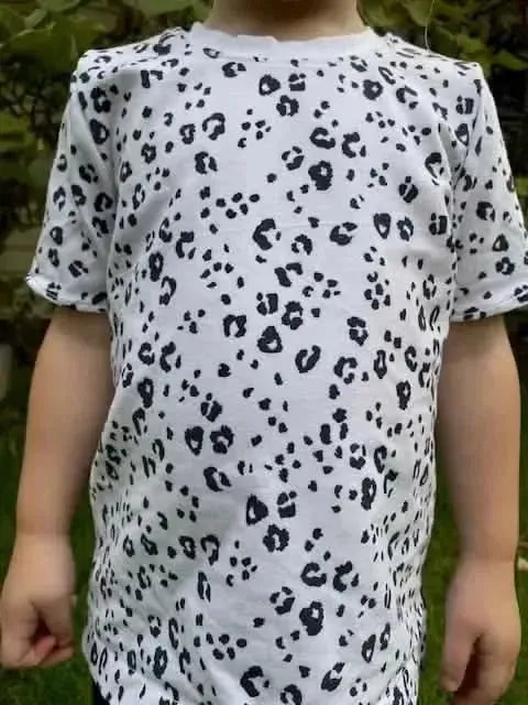White fabric with black leopard print pattern, shown on a child model outdoors.