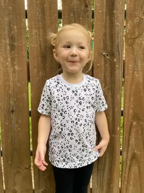 A young child wears a white t-shirt with a black leopard print pattern.