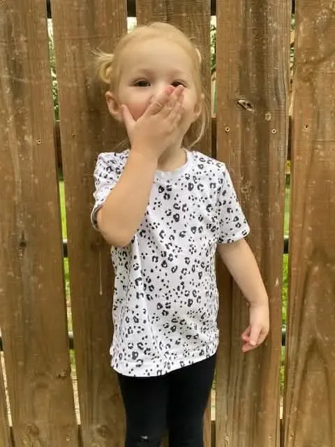 A young child wears a white shirt with a black leopard print pattern.