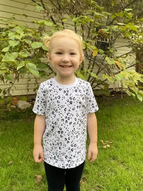 A young child wears a white t-shirt with a black leopard print pattern.