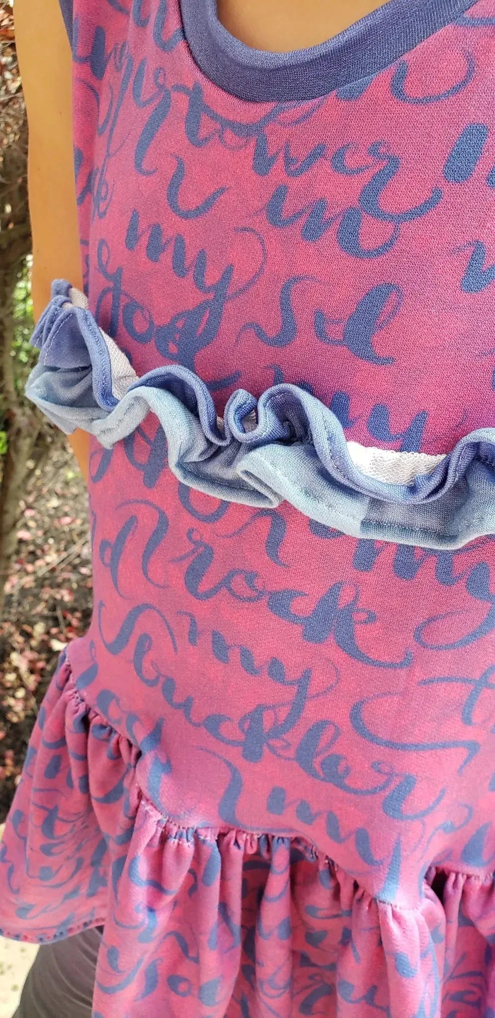 A pink fabric with blue script lettering and ruffled accents.