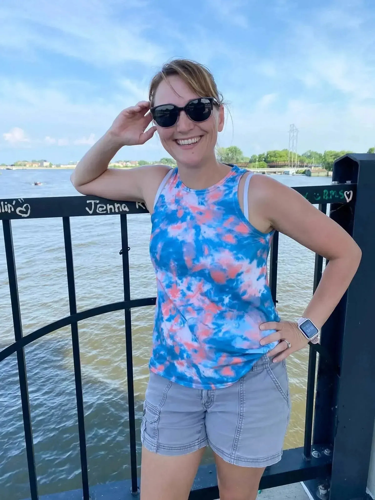 Woman modeling Oceans Edge tie-dye fabric in blue-pink oceanic pattern with tank top and shorts by water.