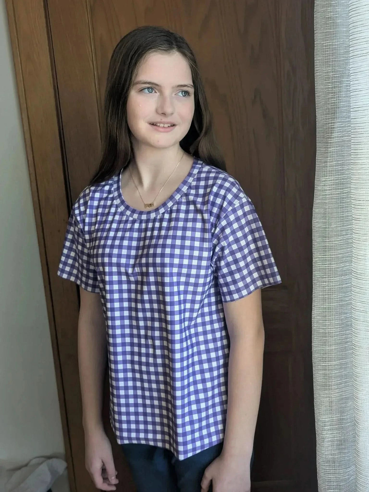 A young girl wears a violet and white gingham shirt.