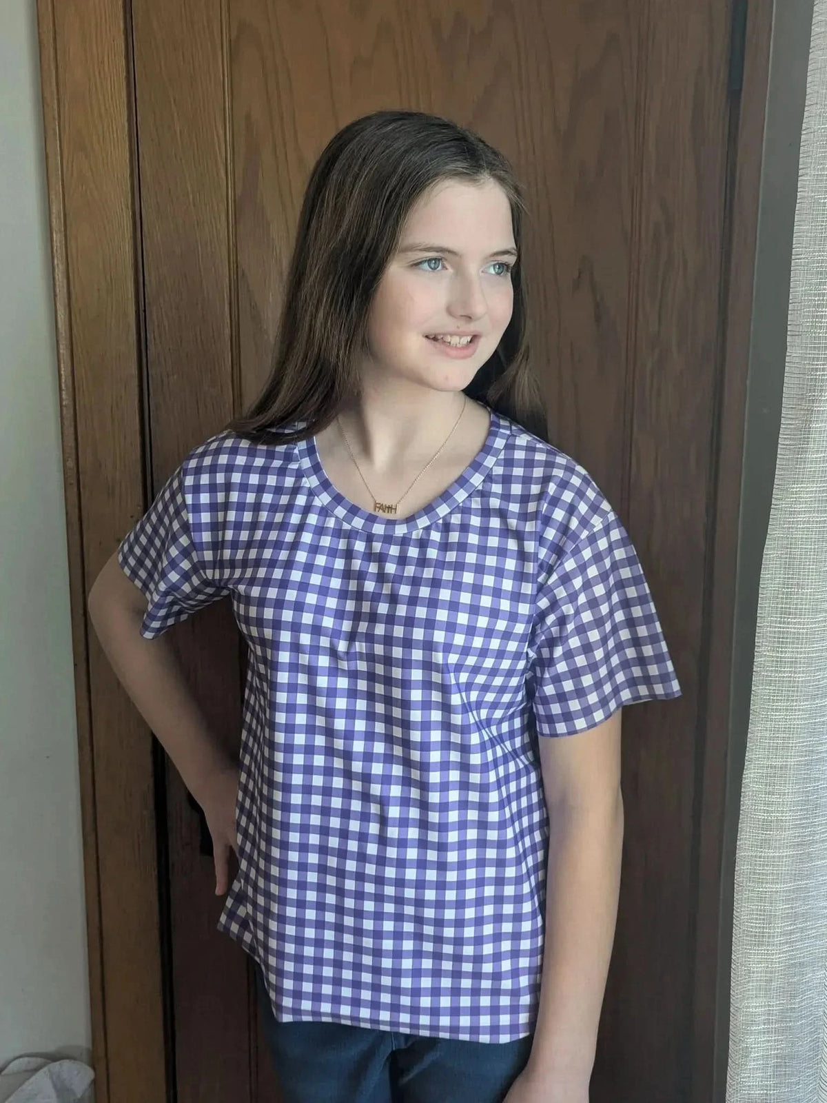 A young girl wears a violet gingham shirt and a "Faith" necklace.