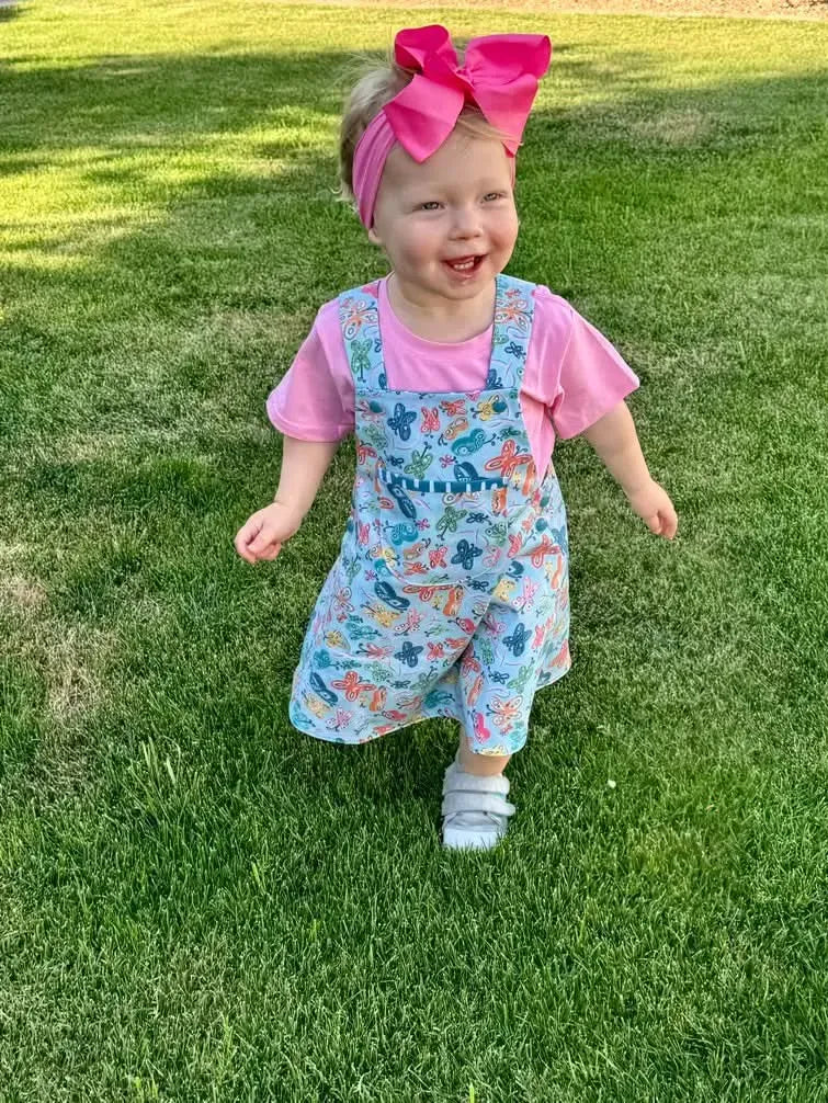A child wears a dress with a painted butterfly pattern over a pink shirt.