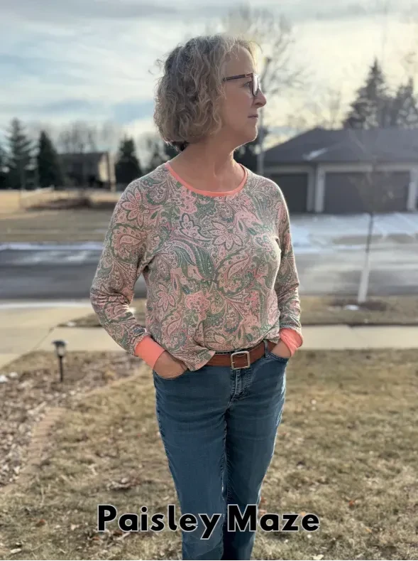 A woman wears a long-sleeved paisley top with jeans and a brown belt.