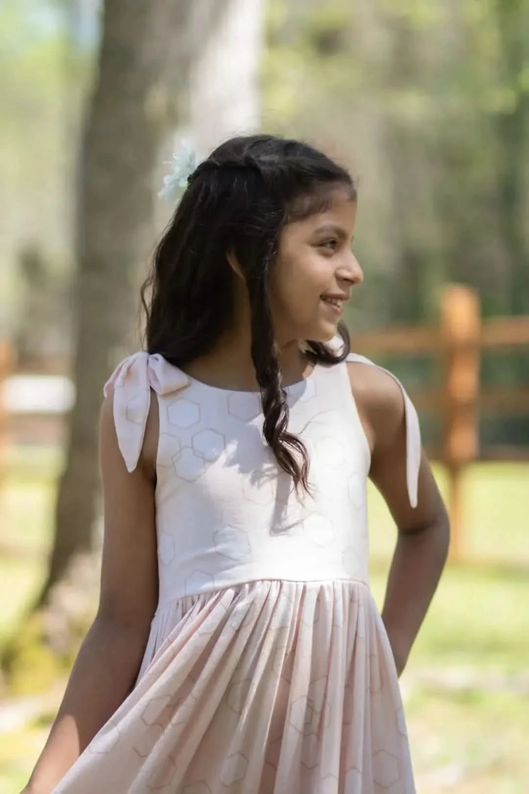 A young girl in a peachy geo print dress with shoulder ties.