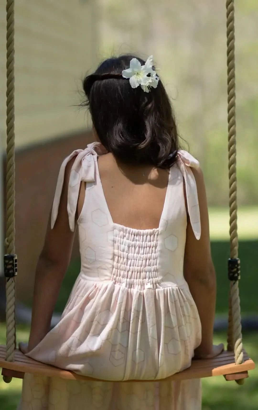 A person from behind wearing a peachy geo dress with a white flower in their hair.
