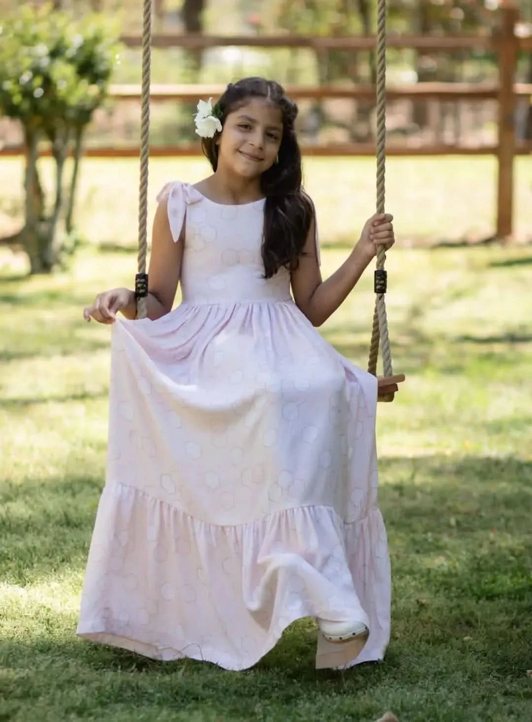 A girl in a light pink dress with a geometric pattern sits on a swing.