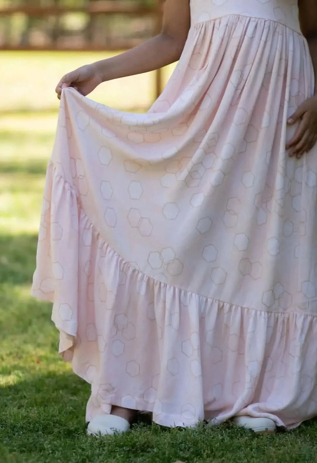 A person in a peachy geo print dress with a ruffled hem stands on grass.