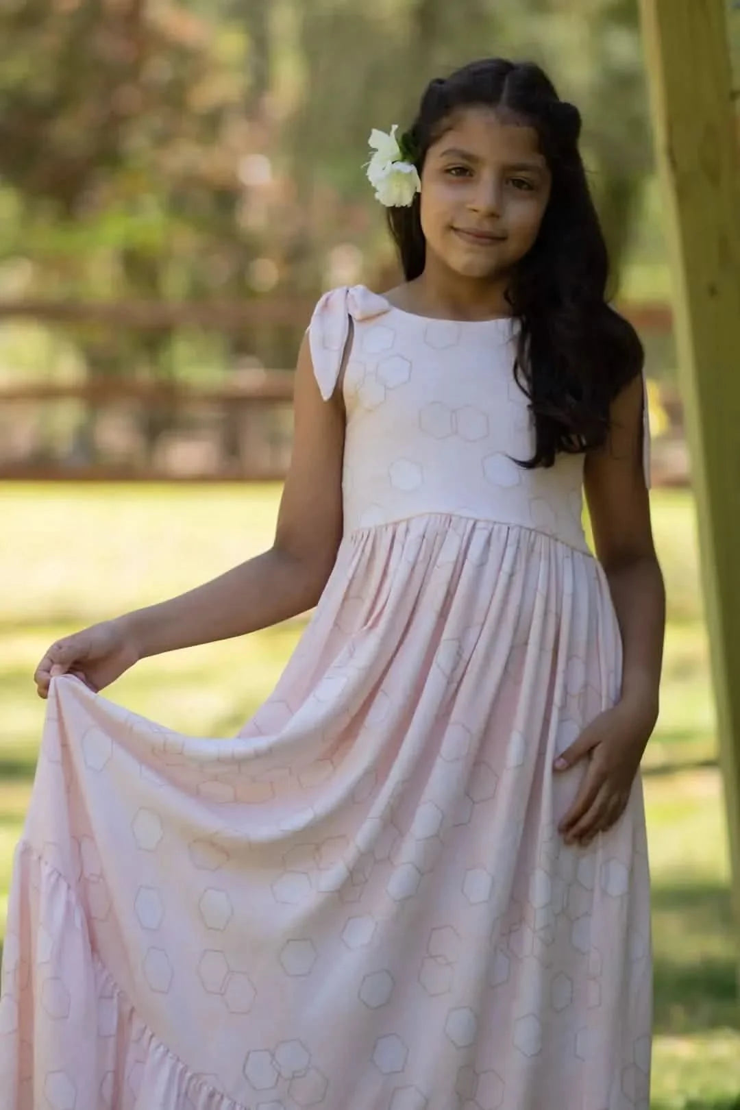 A young girl in a light pink dress with geometric patterns and a white flower in her hair.