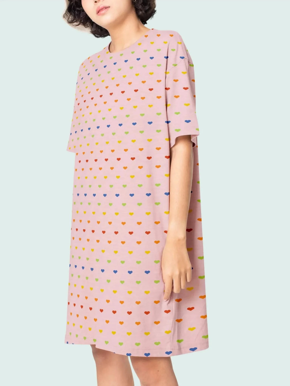 A person wears a pink dress with a rainbow heart pattern.
