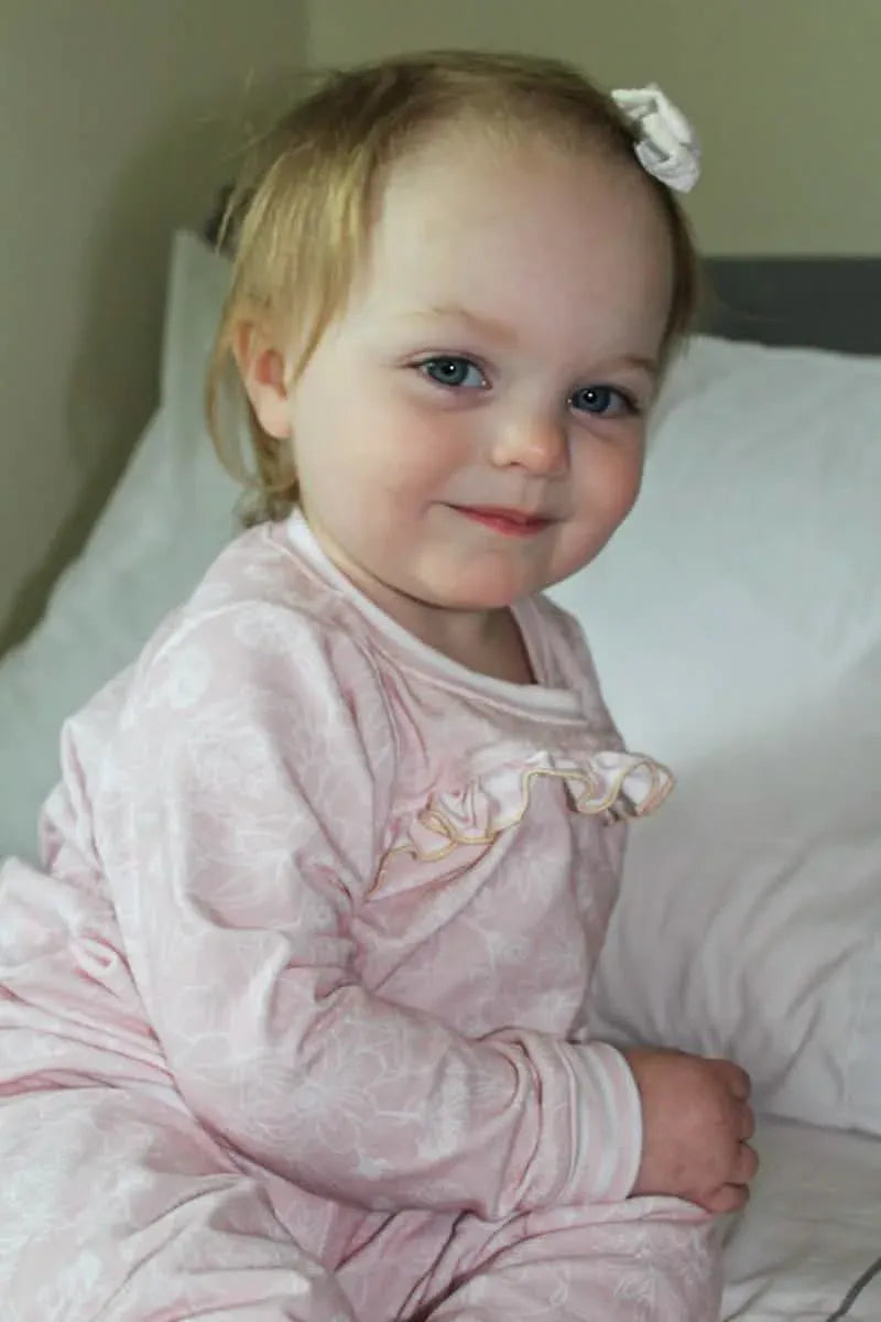 A young child wears pink stenciled floral pajamas with a ruffled neckline.