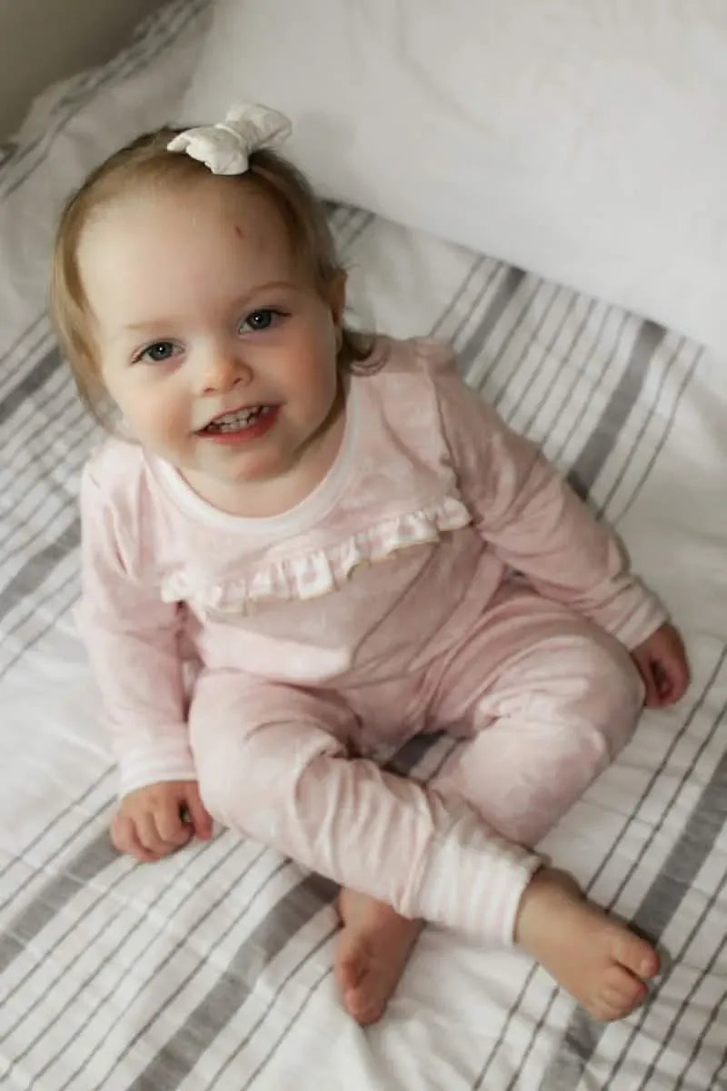 A baby in pink stenciled floral pajamas sits on a striped bed.