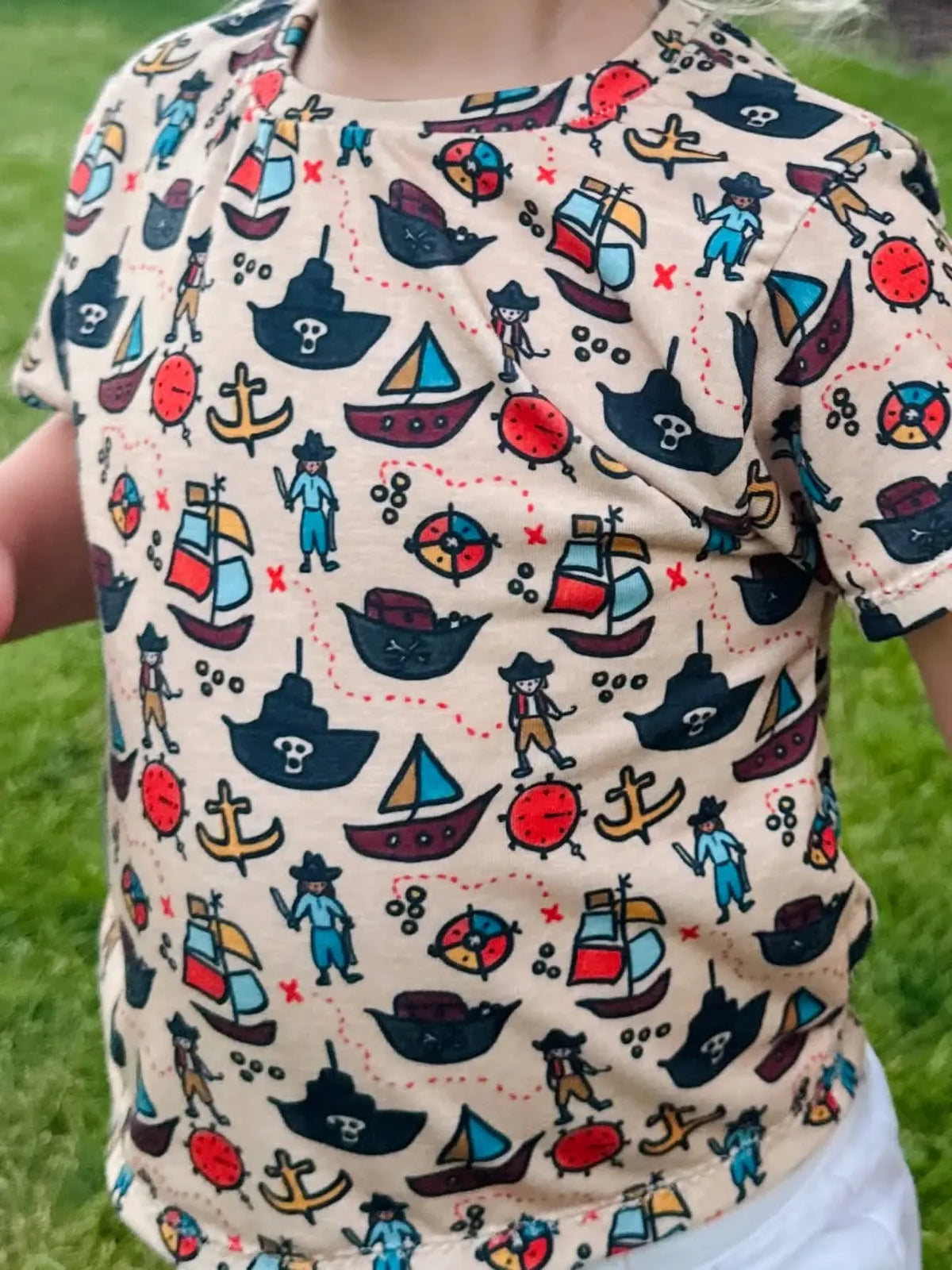 A child wears a beige shirt with a colorful pirate-themed pattern.