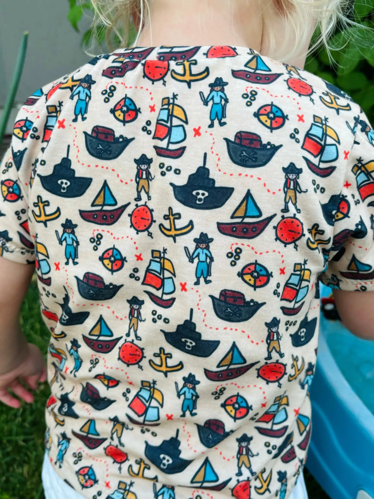 A child wears a pirate-themed shirt with ships, anchors, and pirates.