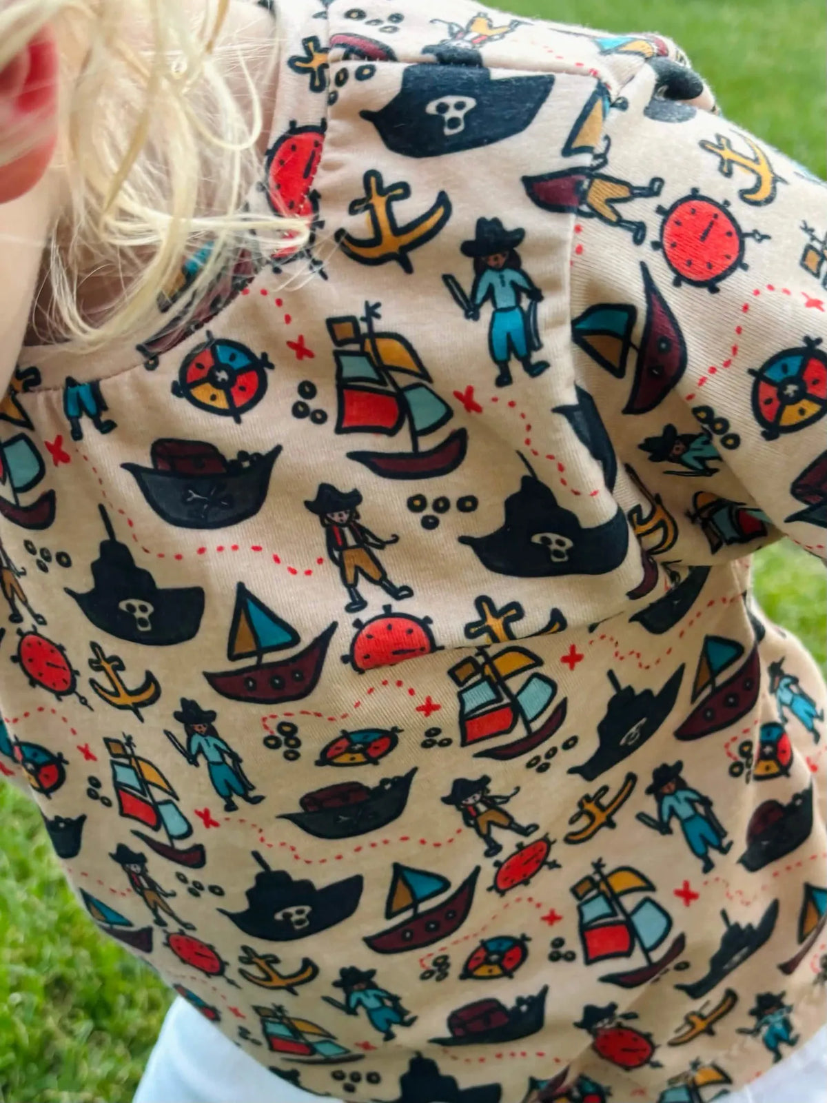 A child wears a pirate-themed shirt with ships, anchors, and treasure maps.