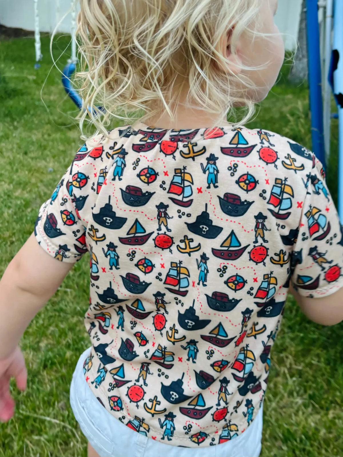 A child wears a beige shirt with a colorful pirate-themed pattern.