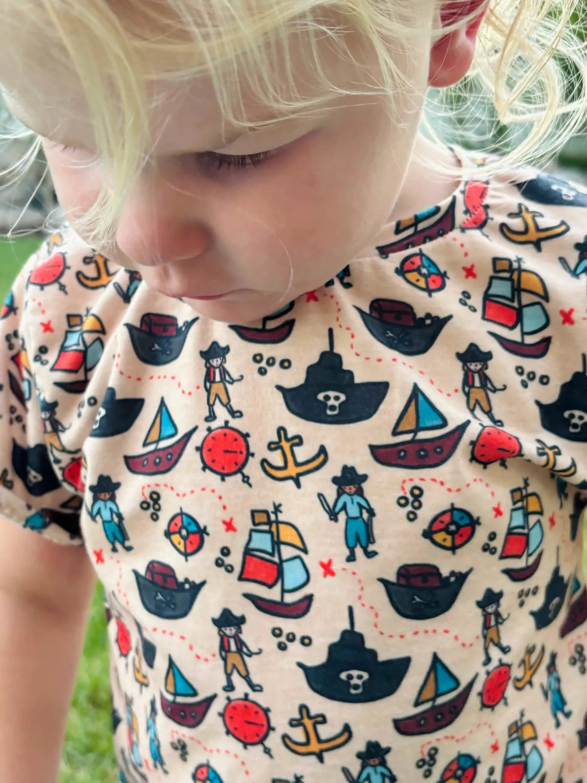 Child wearing a pirate-themed shirt with ships, anchors, and pirates.