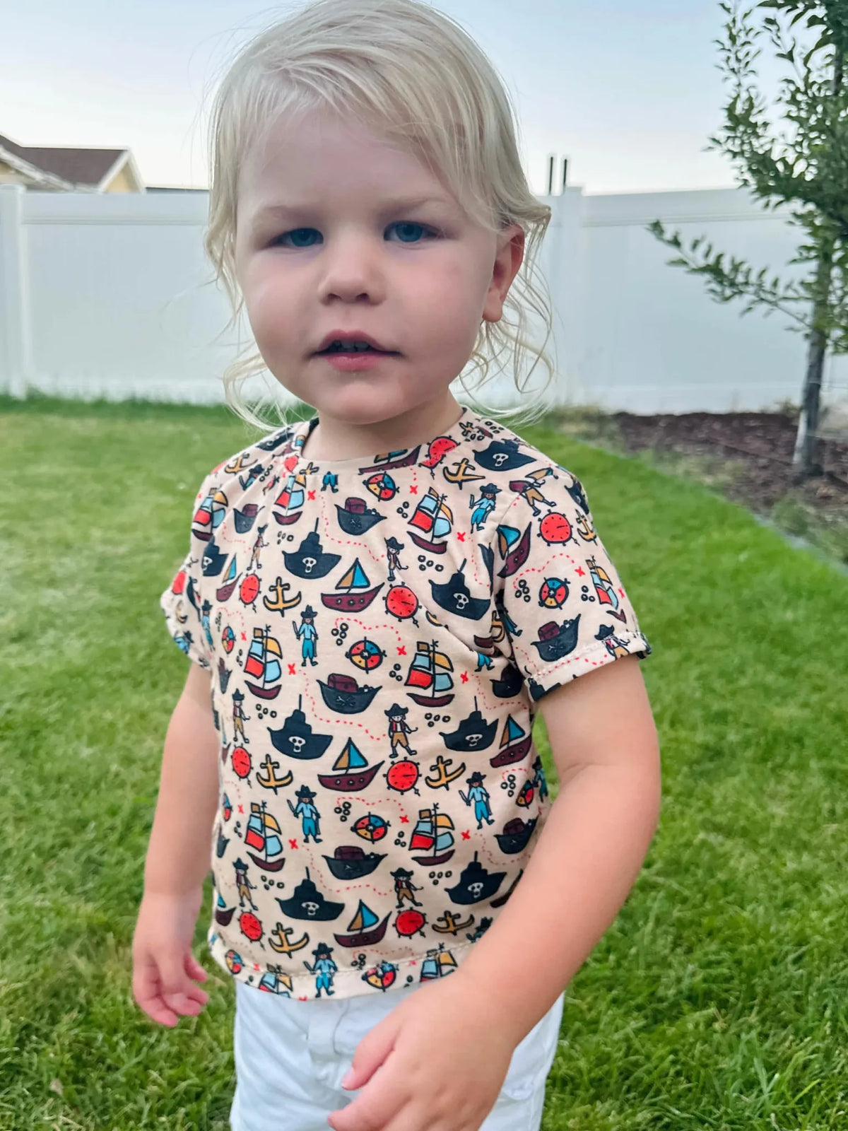 A child wearing a pirate-themed shirt with ships, anchors, and pirates.