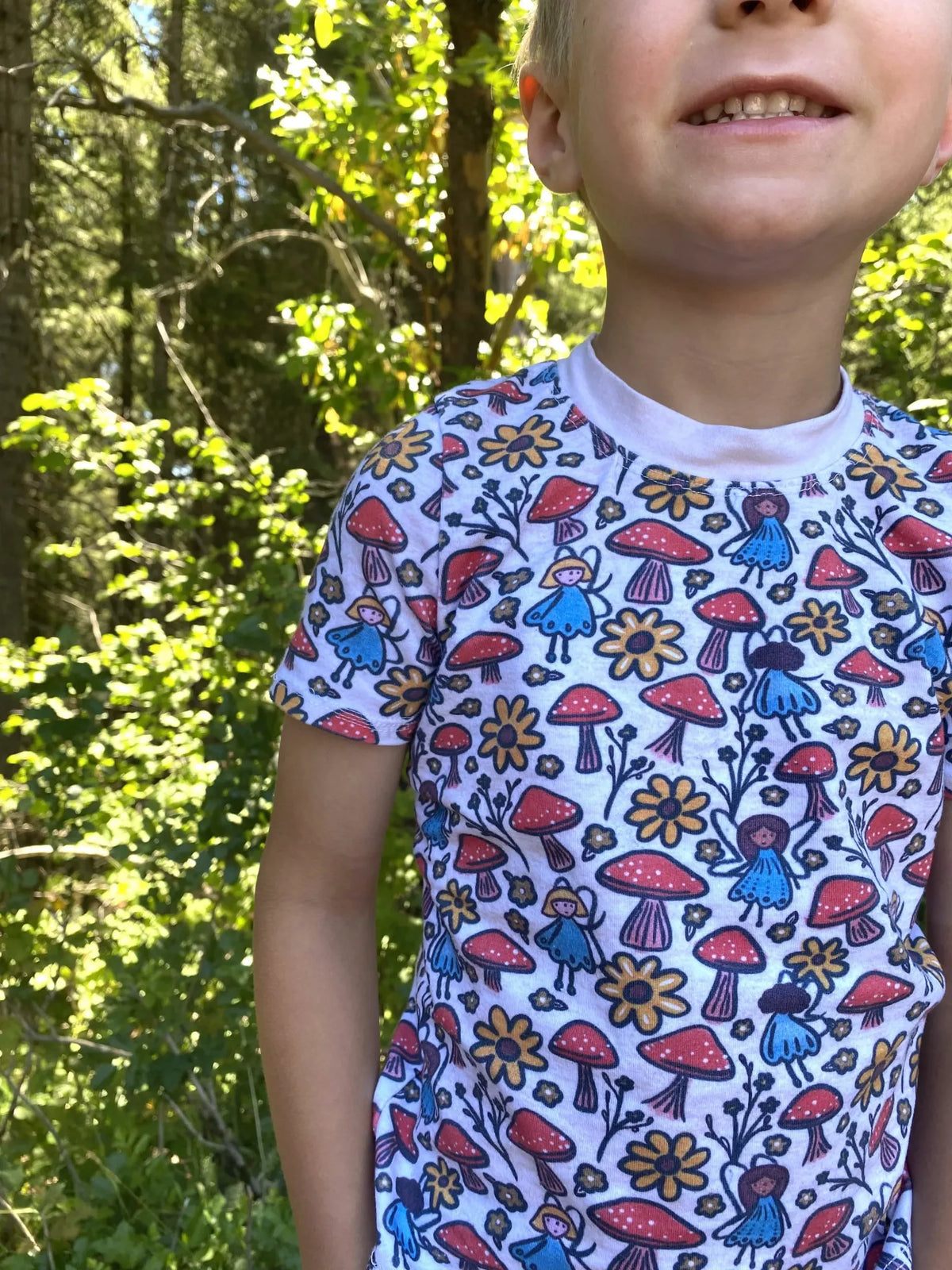 Child wearing a white shirt with a colorful mushroom and fairy pattern.