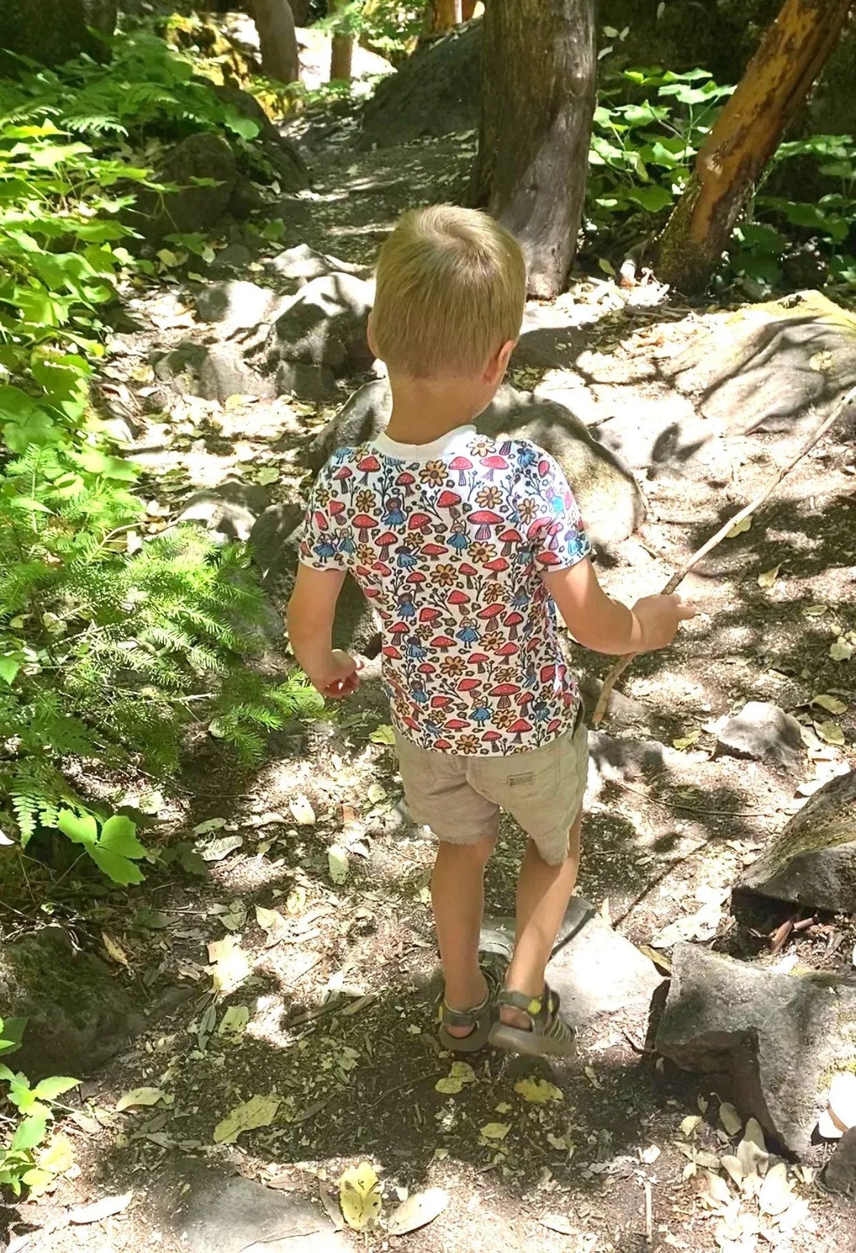 A child from behind wearing a white shirt with a colorful mushroom and flower pattern.