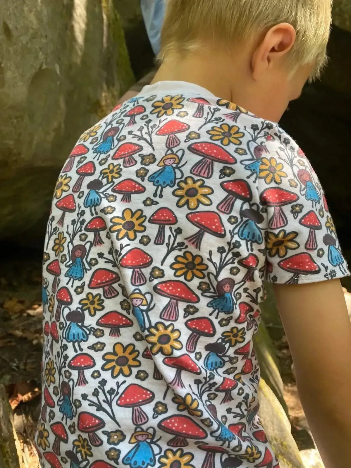 Fabric with whimsical print of fairies, mushrooms, and flowers in red, yellow, and blue.