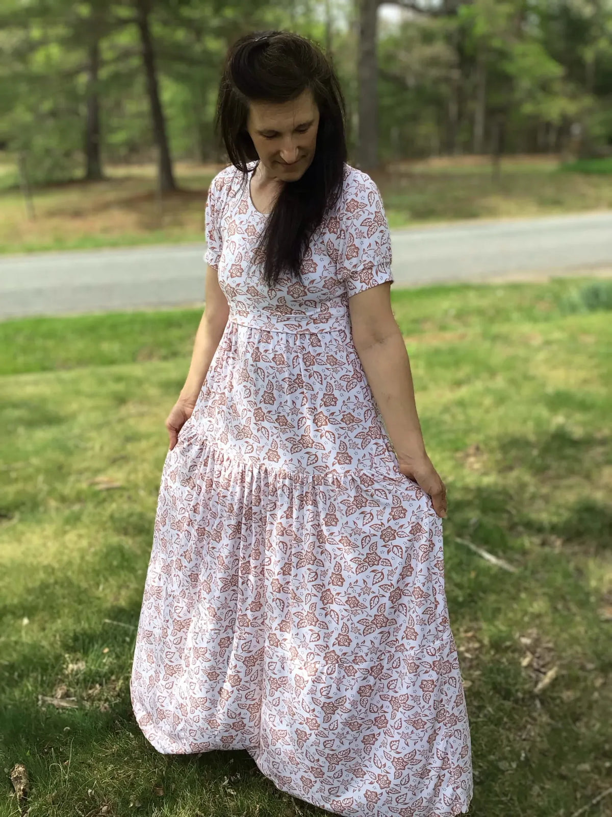 A woman in a white dress with a brown floral pattern stands outdoors.
