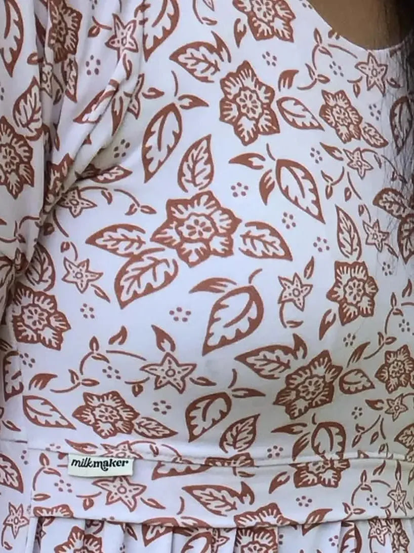 A person wears a white dress with a brown folk flower pattern.