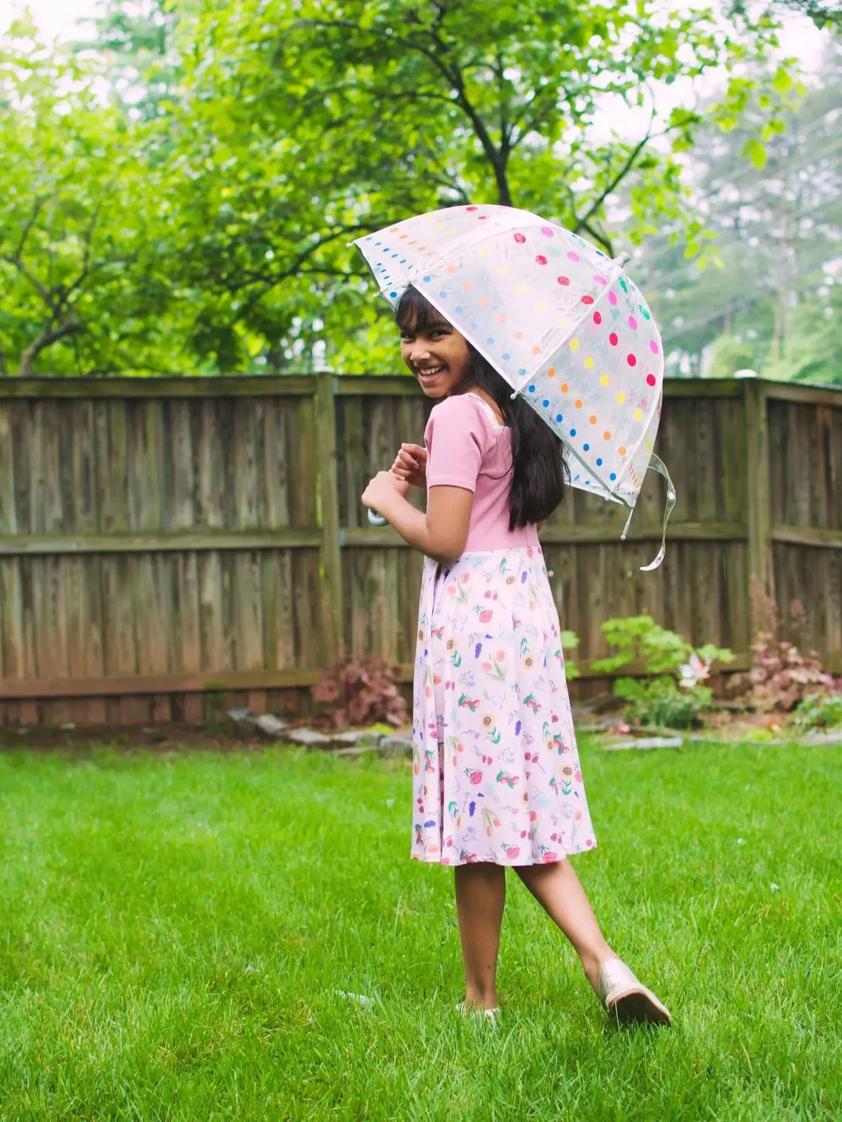 Pink floral fabric with butterfly garden theme on a wooden fence and green grass.