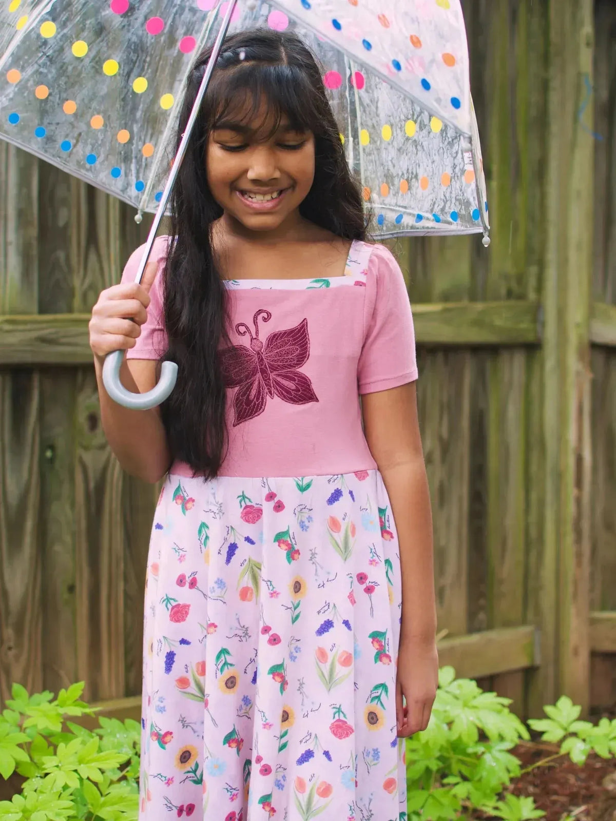 Pink floral fabric with butterfly garden theme, featuring flowers and butterflies.