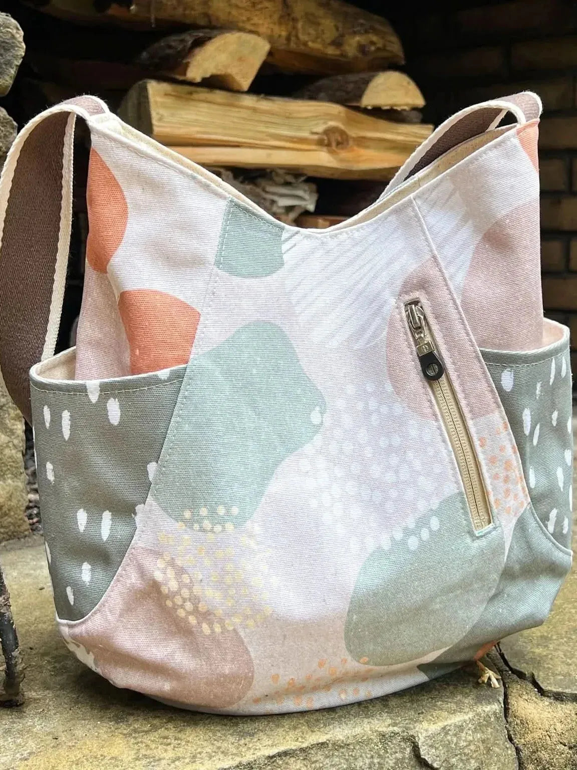 A fabric tote bag with abstract shapes in green, pink, and white, and a zipper pocket.