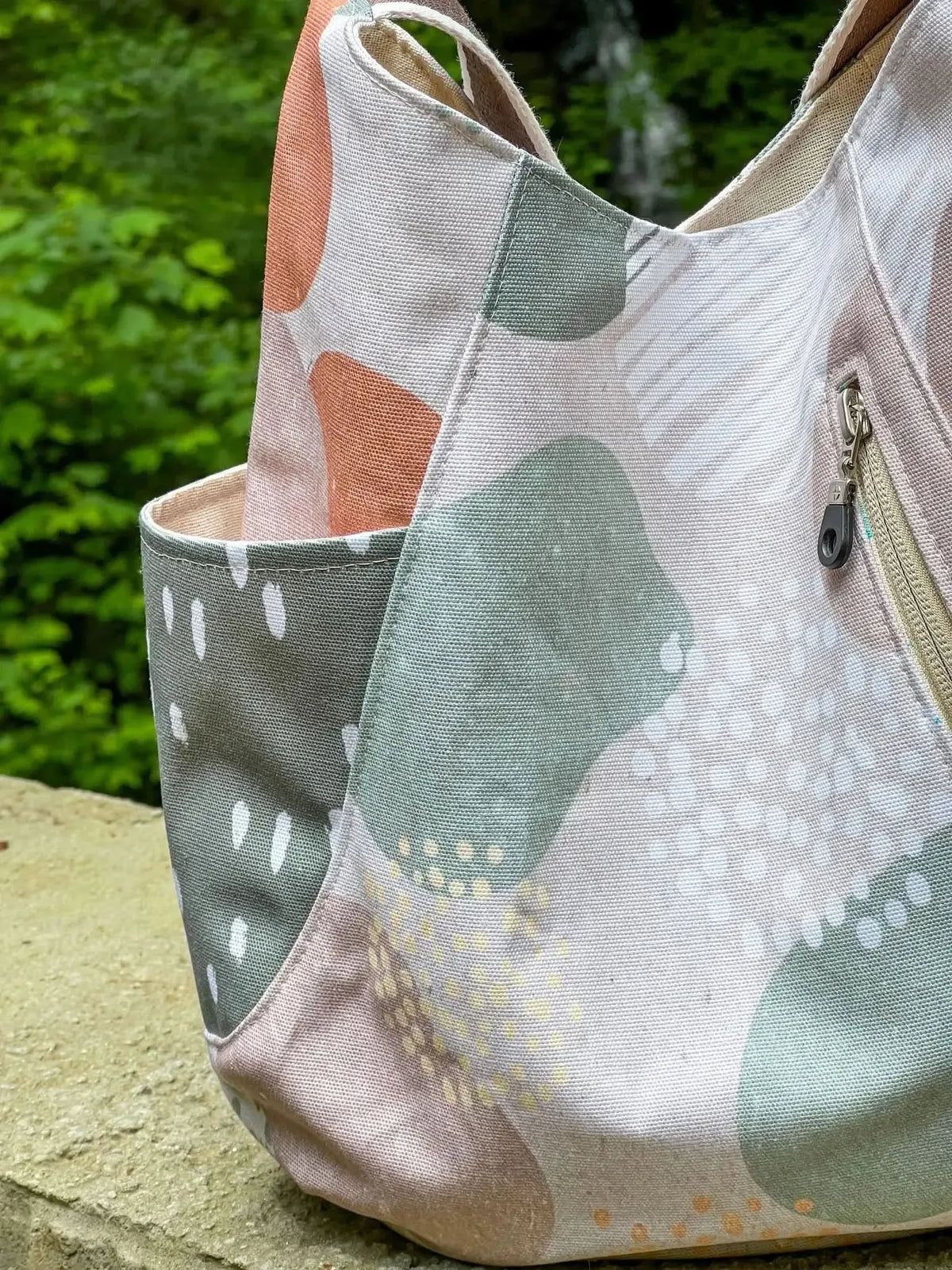A canvas bag with abstract shapes in green, orange, and white, and a zippered pocket.