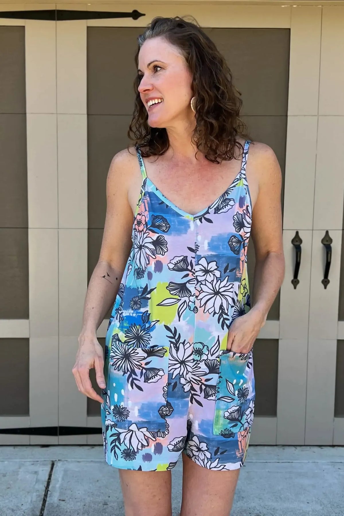A woman smiles, wearing a blue graffiti floral print romper with pockets.