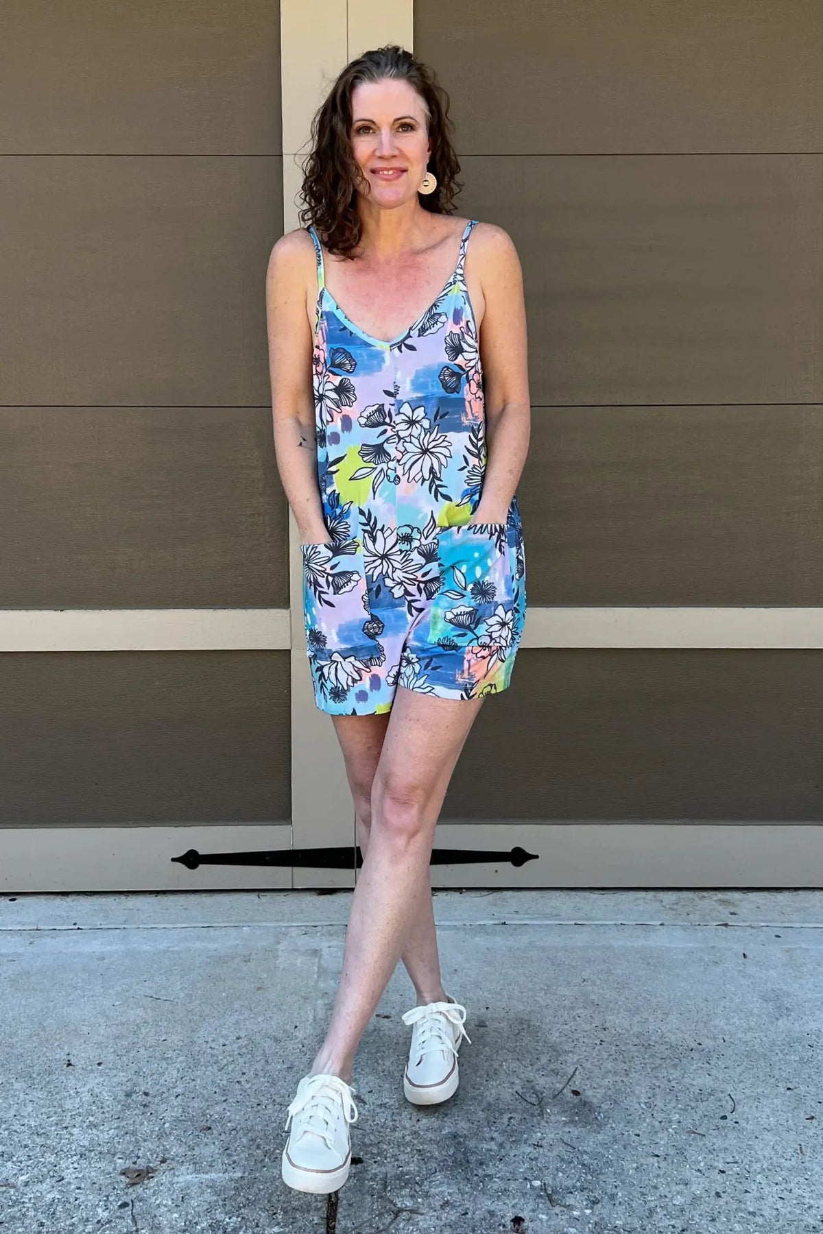 Woman in a blue graffiti floral romper with pockets and white sneakers.