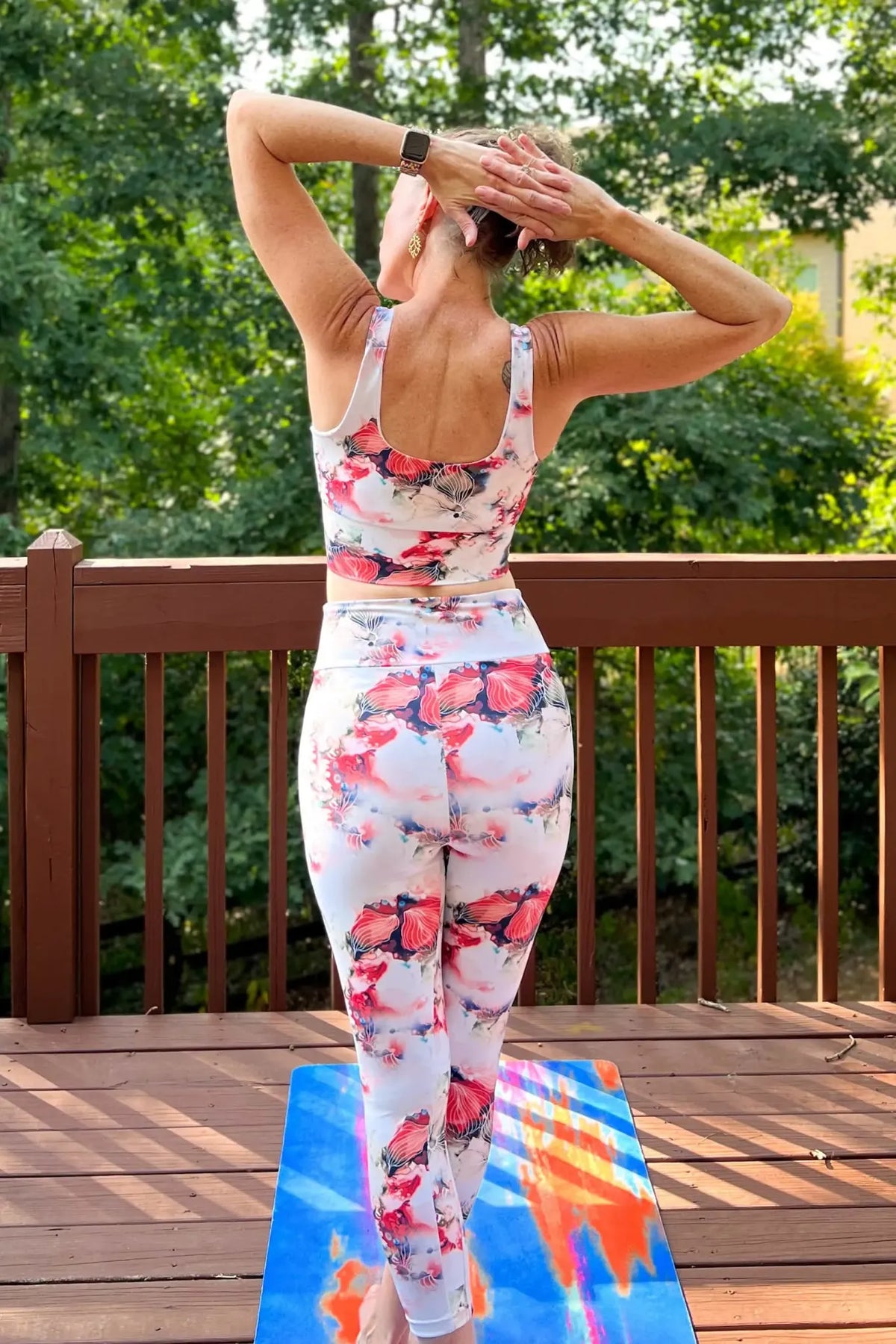 A woman from behind wears a white floral sports bra and leggings on a deck.