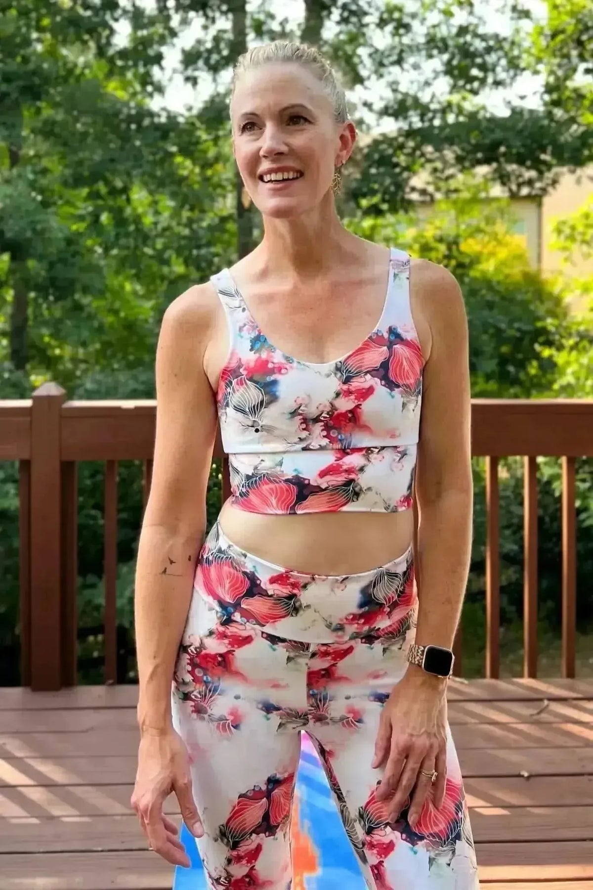 Woman modeling white athletic outfit with red floral print on deck.