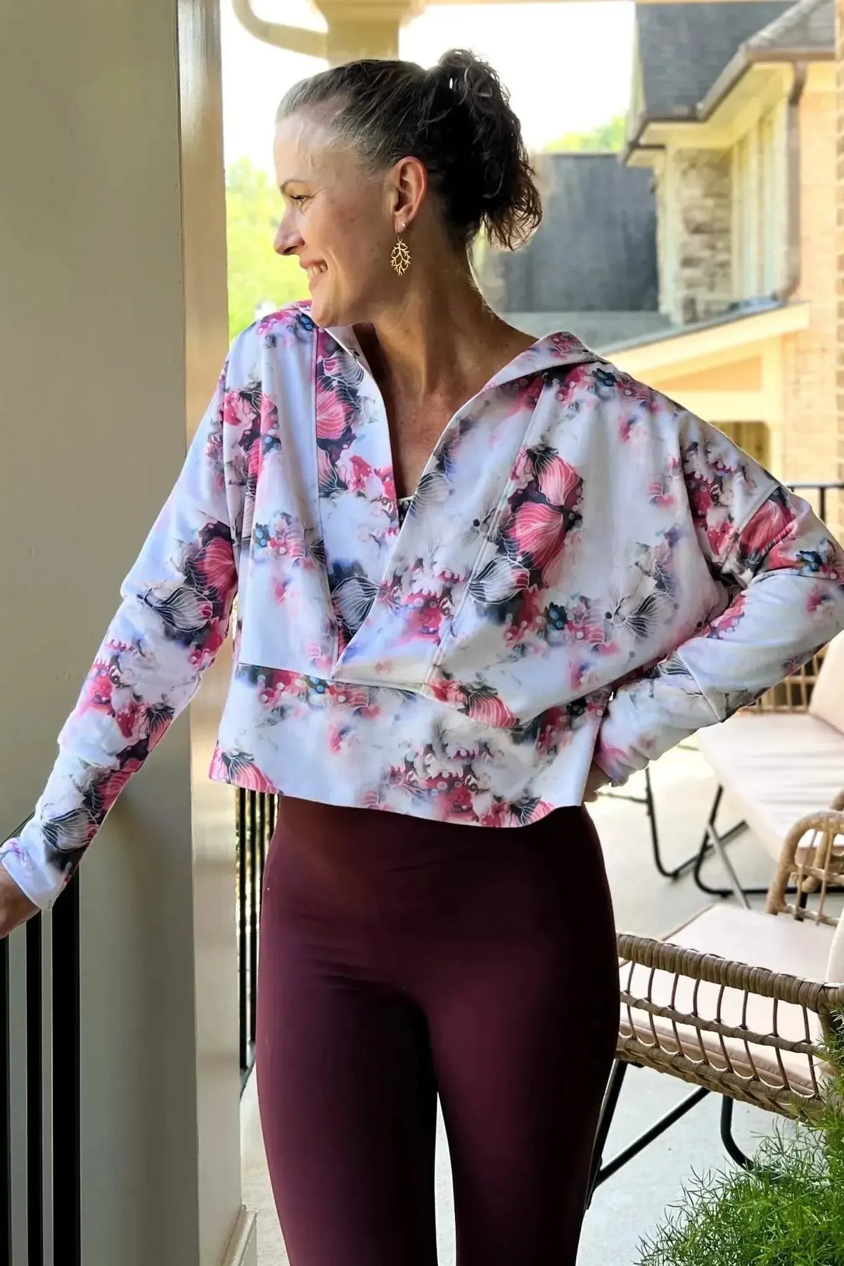 Woman modeling a floral wrap top in pink and white with maroon leggings on a porch.