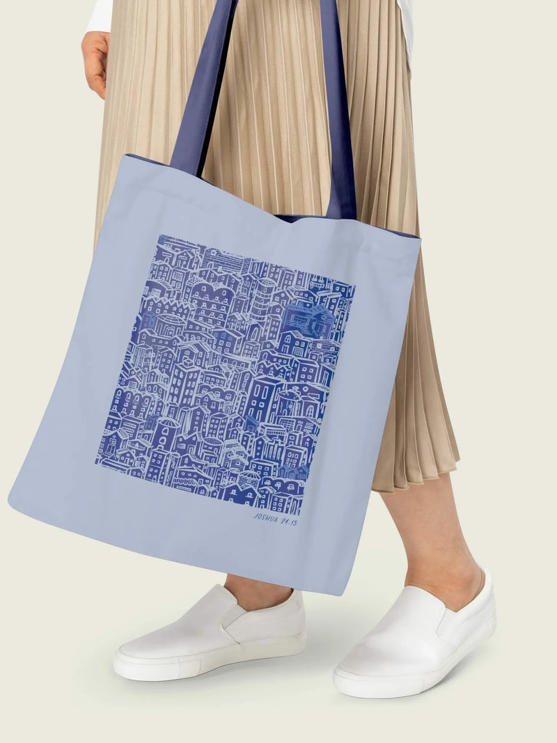 A person holds a light blue tote bag with a blue and white city illustration.