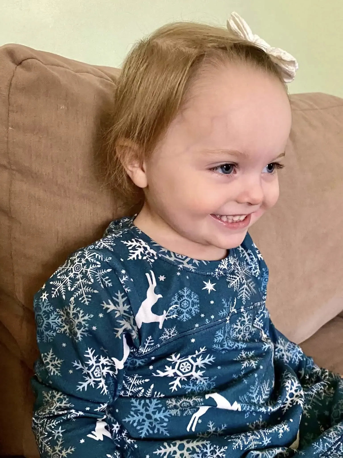 A smiling child in a blue shirt with white reindeer and snowflake patterns.
