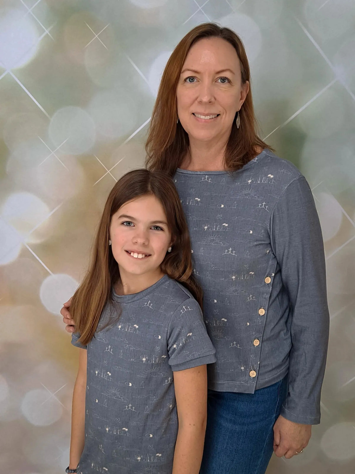 Two females wearing matching blue shirts with a subtle pattern of crosses and landscapes.
